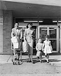 1950s FAMILY OF FOUR WALKING OUT OF GROCERY STORE FATHER PUSHING SHOPPING CART MOTHER AND SON CARRYING BAGS