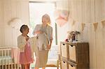 Pregnant mother and daughter holding baby clothes in nursery