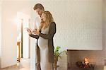 Pregnant couple using digital tablet near fireplace in living room