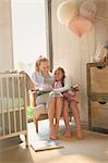 Pregnant mother and daughter reading story book in nursery