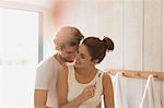 Affectionate couple brushing teeth in sunny bathroom