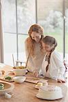 Pregnant mother and daughter preparing food at dining table