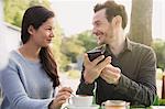 Couple with cell phone drinking coffee at outdoor cafe