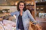 Portrait smiling woman with basket leaning on cheese display case in market