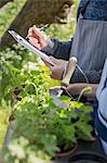 Close up plant nursery workers with clipboard and potted herbs