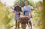 Portrait smiling plant nursery workers with wheelbarrow and flowers in sunny garden