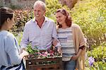 Plant nursery worker helping smiling couple with flowers in garden