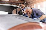 Focused mechanic examining classic car panel in auto repair shop