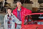 Portrait smiling father and son next to classic car in auto repair shop