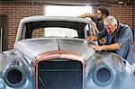 Mechanics rebuilding classic car in auto body shop
