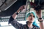 Young female mechanic with blue hair fixing car in auto repair shop