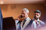 Tailor fitting businessman on cell phone for suit in menswear shop