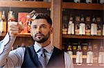 Serious well-dressed bartender examining whiskey