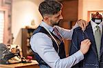 Tailor adjusting suit on dressmakers model in menswear shop