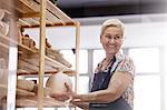 Smiling senior woman placing pottery vase on shelf in studio