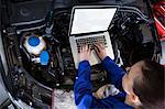 Female mechanic using a digital tablet while servicing car engine at the repair garage