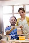 Mature couple photographing pottery vase with camera phone in studio