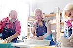 Smiling senior couple using pottery wheels in studio