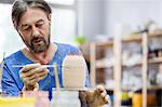 Focused mature man painting pottery vase in studio