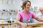 Smiling mature woman rolling clay with rolling pin in pottery studio