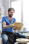 Mature man holding bowl at pottery wheel in studio