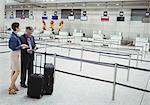 Business people waiting at check-in counter with luggage in airport terminal