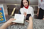 Passenger giving a passport and mobile phone to an airline check-in attendant at check-in counter