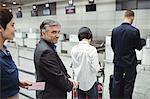 Passengers waiting in queue at a check-in counter with luggage inside the airport terminal