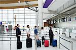 Passengers waiting in queue at a check-in counter with luggage inside the airport terminal