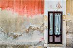 Worn, stone walls of a building with curtained door in Ragusa in Sicily, Italy