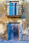 Worn, peeling stone walls on building with wooden doors and balcony in Ragusa in Sicily, Italy