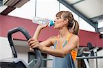 Young woman drinking water while exercising on a machine in gym