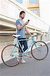 Young man using a mobile phone with bicycle outdoors