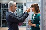 Shop assistant helping customer for trying on eyeglasses in optical shop