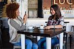 Young woman taking a picture of her friend with smartphone at cafe