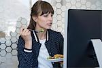 Beautiful woman sitting in front of computer and eating lunch