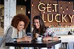 Female friends using a smart phone with coffee at cafe