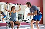 Young woman exercising with dumbbells with his trainer assisting her