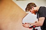 A furniture workshop making bespoke contemporary furniture pieces using traditional skills in modern design. A  man using a tool on the curved cut out edge of a piece of wood.