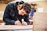 A furniture workshop making bespoke contemporary furniture pieces using traditional skills in modern design. A man marking a piece of wood with a pencil.
