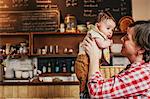 A woman holding up a young baby at a coffee shop.