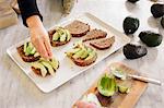 A woman preparing open sandwiches with brown bread and avocado.