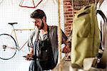 A man working in a bicycle repair shop looking at his smart phone.