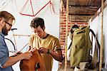 Two men in a cycle repair shop, a client looking at backpacks and bike packs.