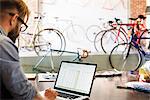 A man in a bicycle repair shop using a laptop computer.  Running a business.