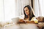 Senior woman with long brown hair sitting on a sofa, using a digital tablet.