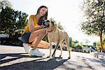 Senior woman wearing shorts, kneeling in the street, stroking a dog.