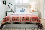 A bedroom in an apartment with a double bed and a retro look antique patterned patchworked bed cover.