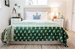 A bedroom in an apartment with a double bed and beside cabinets, and a green fabric patterned bedspread.