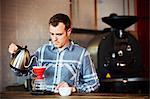 Specialist coffee shop. A man brewing coffee using a filter paper, and drinking it.